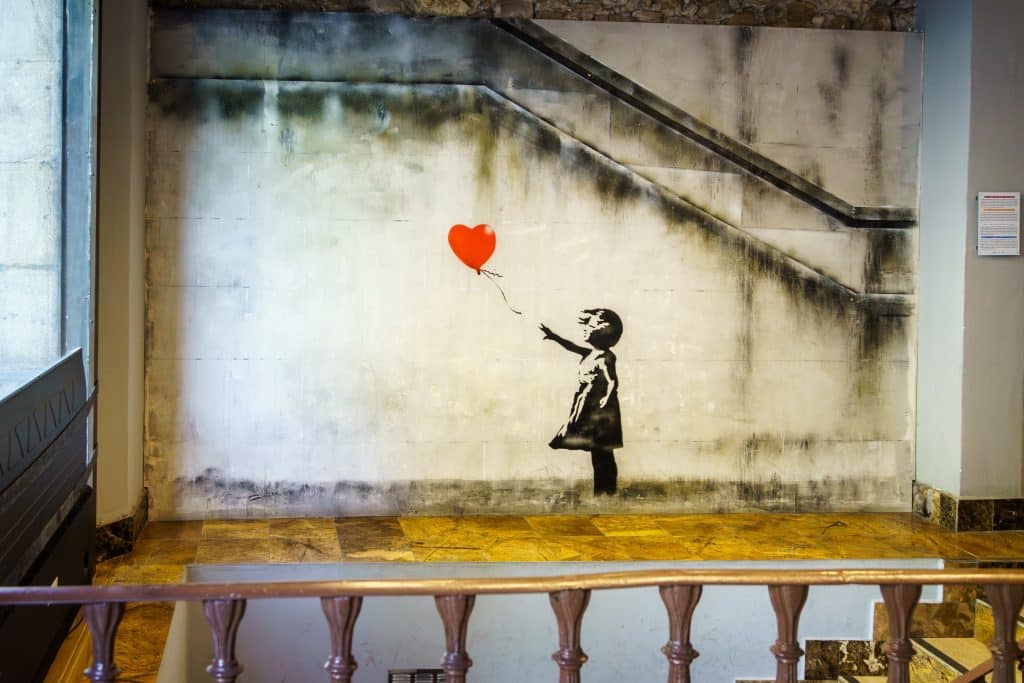 Stencil art of a young girl holding her hand out toward a floating balloon