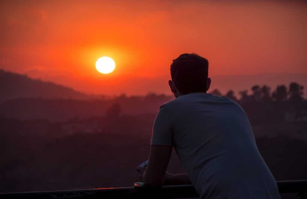 Guy looking off into the orange and red sunset, enjoying the present moment.