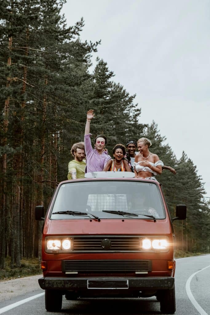 A group of friends hanging out of the roof of a van on a road trip.