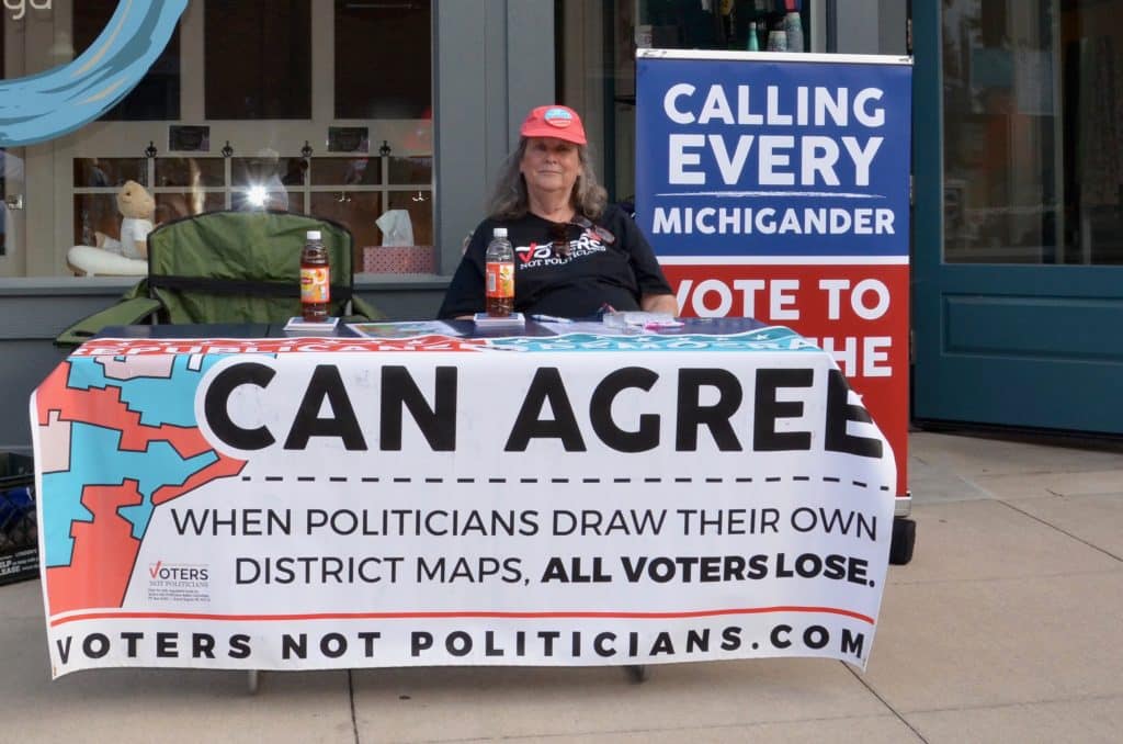 A woman sitting at a table with a sign saying, gerrymandering hurts people