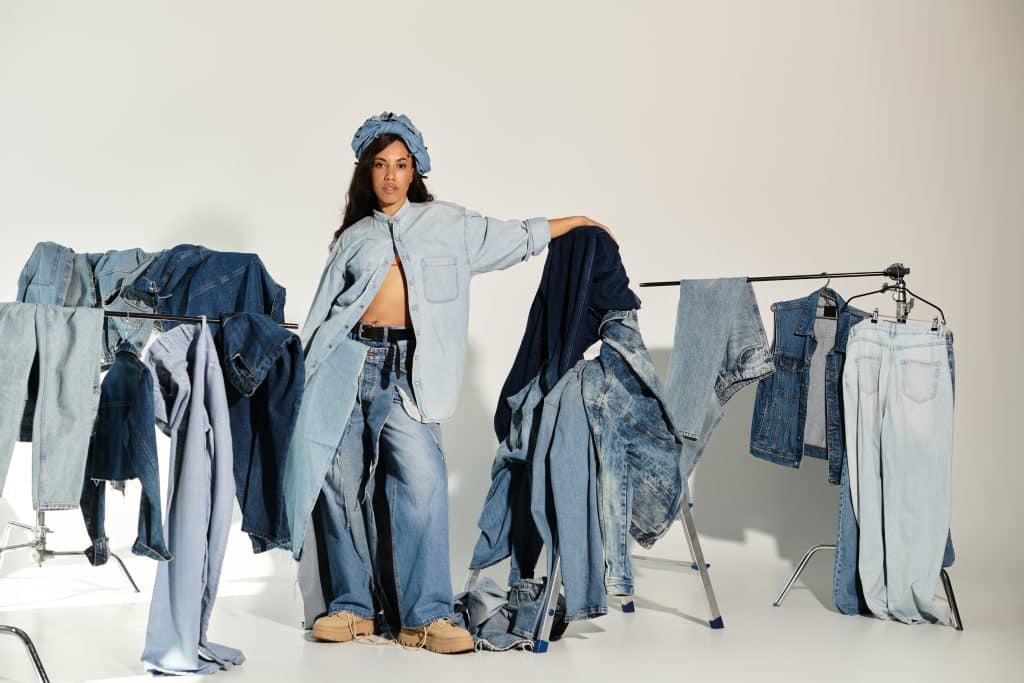 A woman in a denim outfit stands surrounded by other denim clothing.