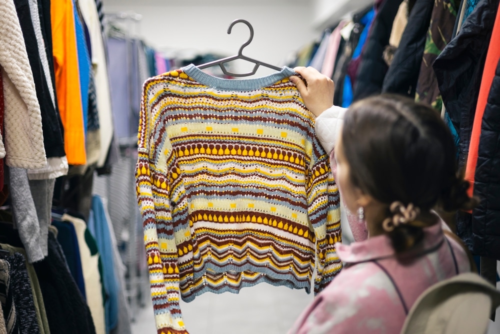 Young woman choosing clothing at a thrift store, sustainable and reused fashion.