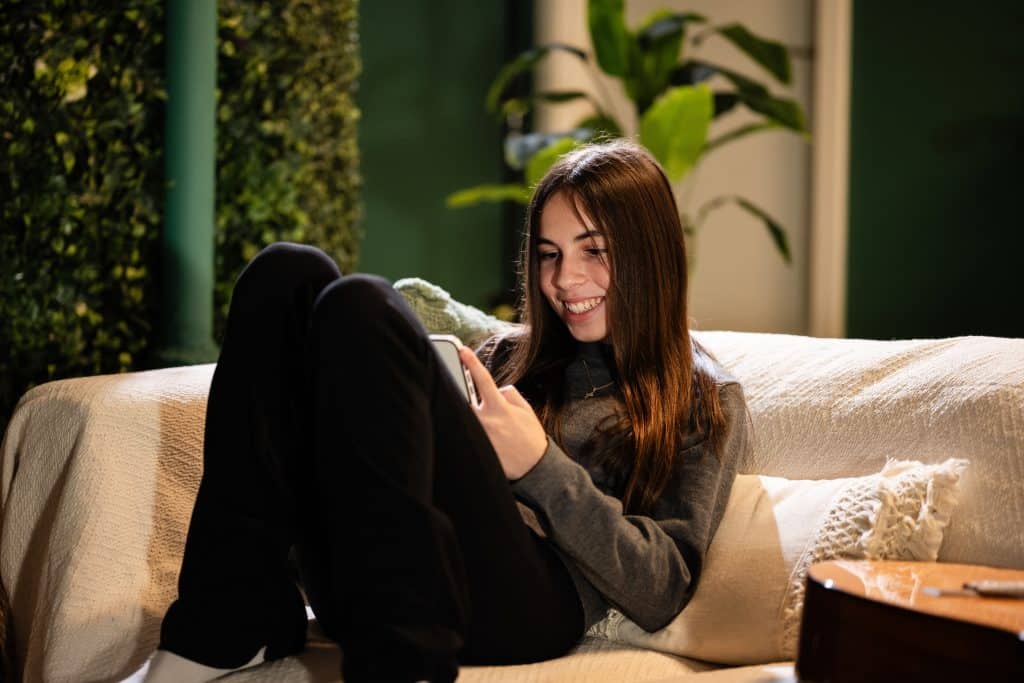 A young woman who is relaxing at home, smiling at her phone screen