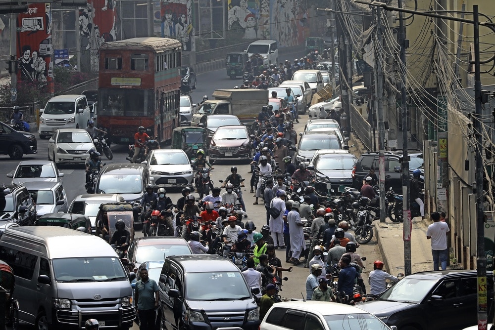 A long line of motorcyclist competing with cars to get to the gas station.