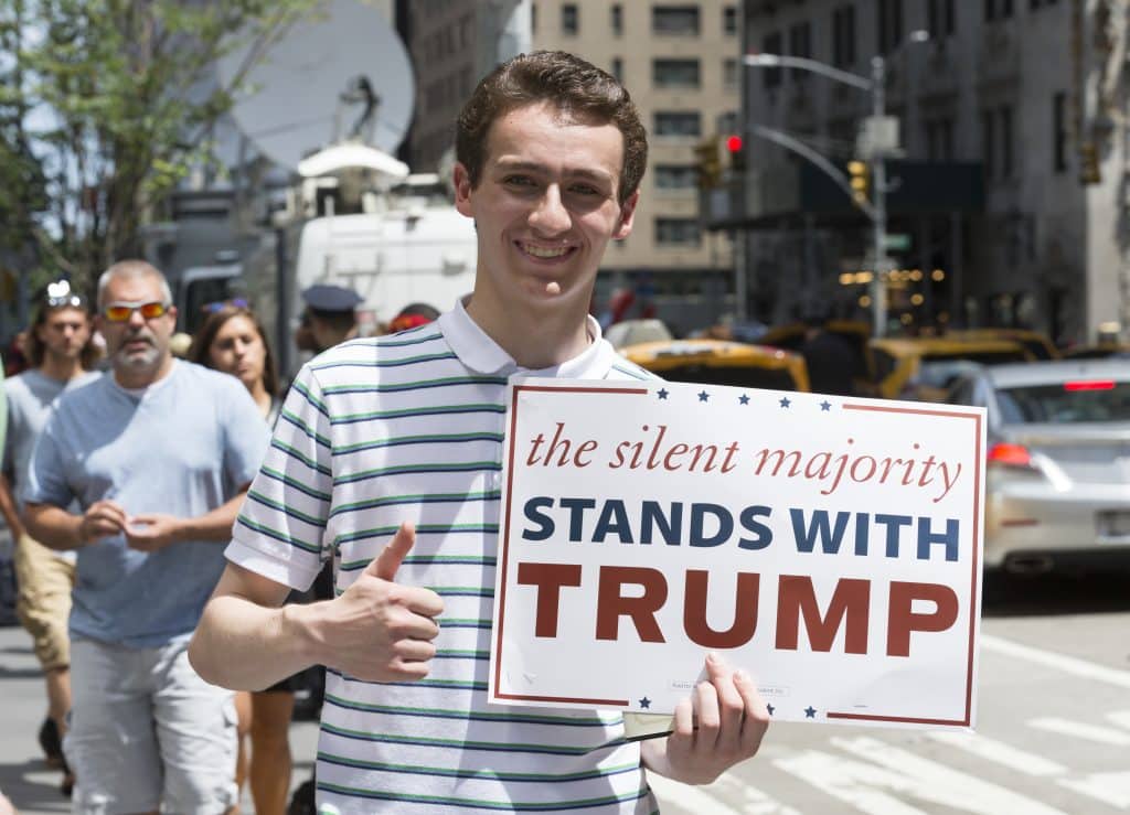Young man holds up sign saying "The Silent Majority Stands With Trump."