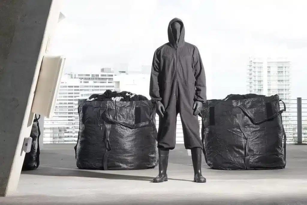 Image of a model wearing a all black outfit from the Yeezy x Gap campaign standing in between 2 clothing bins.