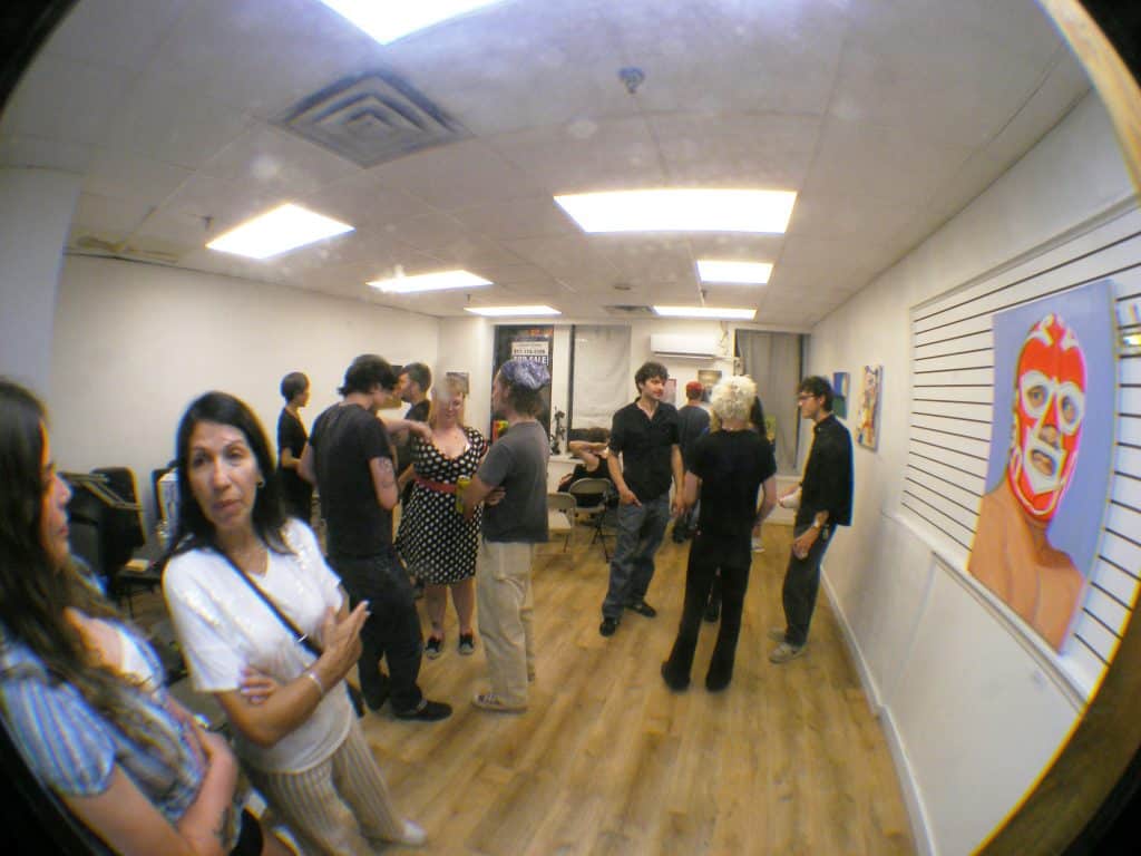 Guests flood into the gallery and begin socializing with one another. Groups gather around different paintings with people peering to get closer looks.
