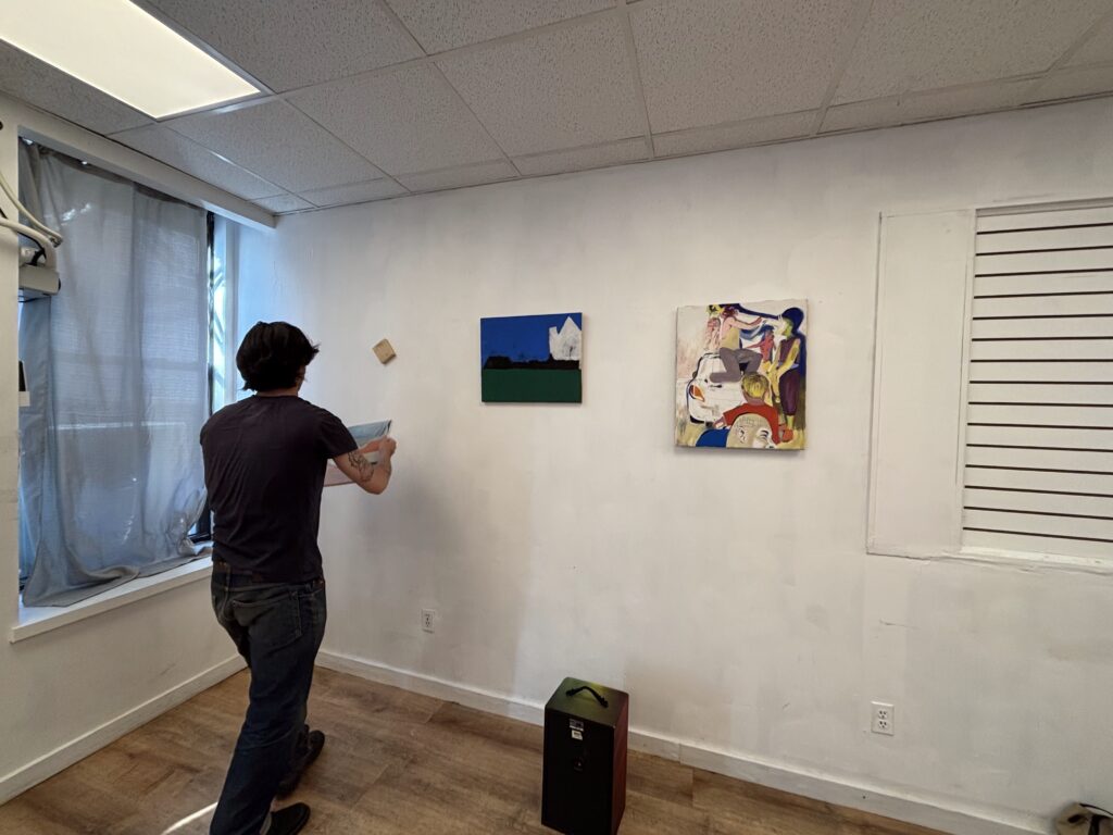 Featured artist, Boris Gross, helps setting up the gallery. He hangs a piece of art in a semi-complete gallery space.