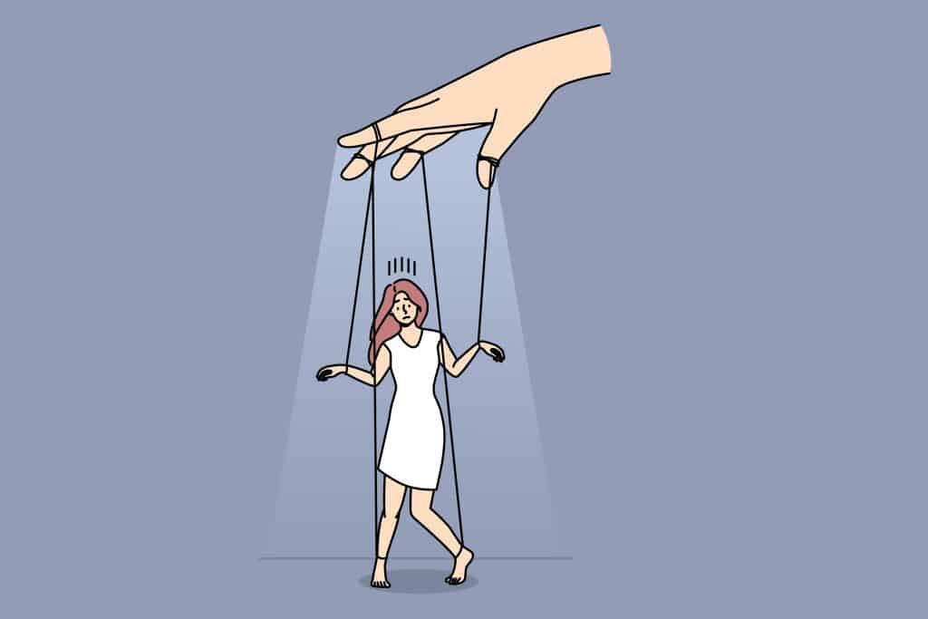 A figure tied to strings being controlled by a hand above; like a puppet