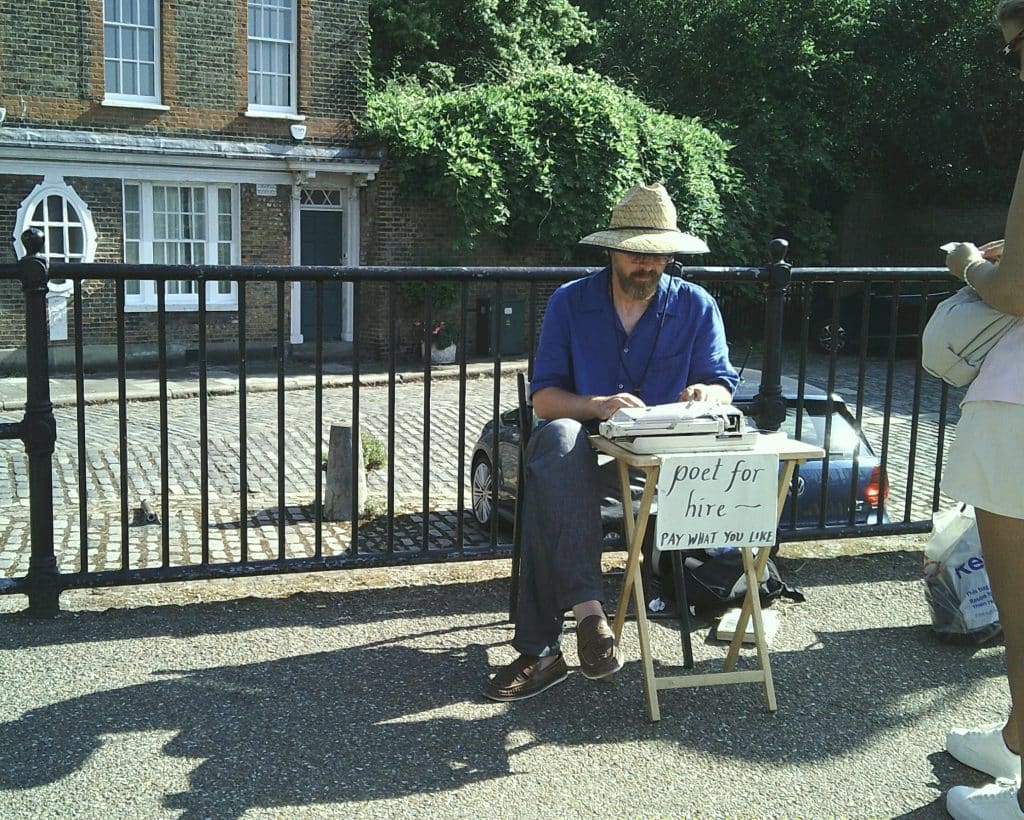 A poet sitting on a desk with a sign "poet for hire," typewriting poems for people on the street.