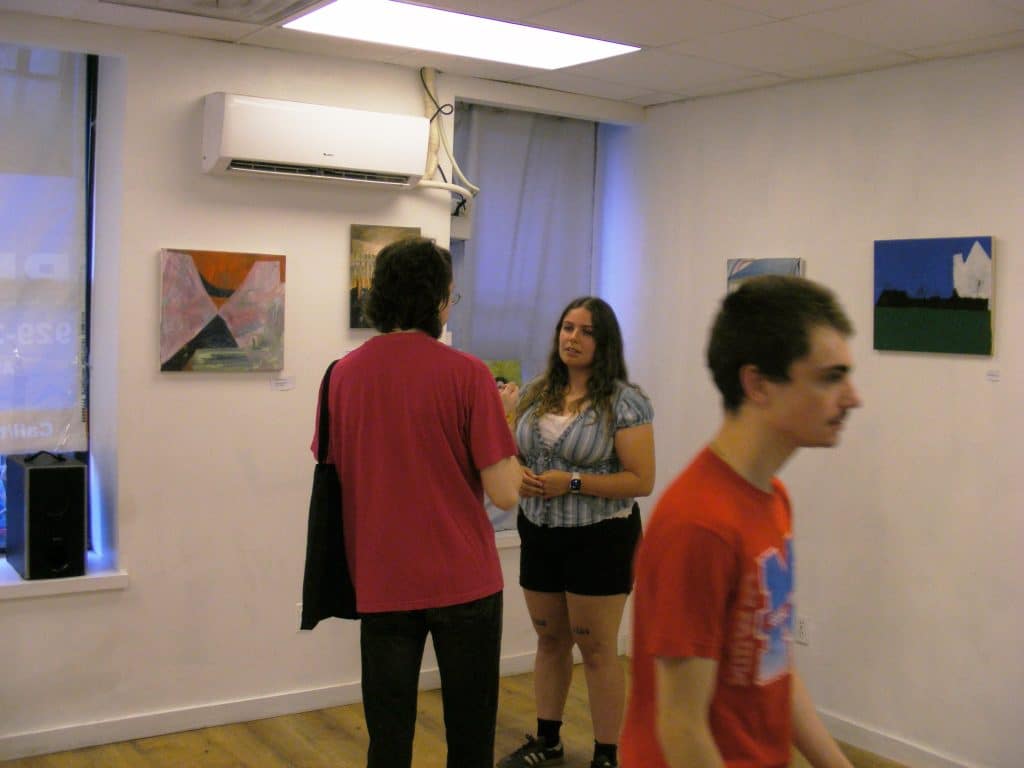 Three featured artists mingle with each other while they wait for the gallery to officially open. They are framed by their own work, hung up, and ready to be seen.