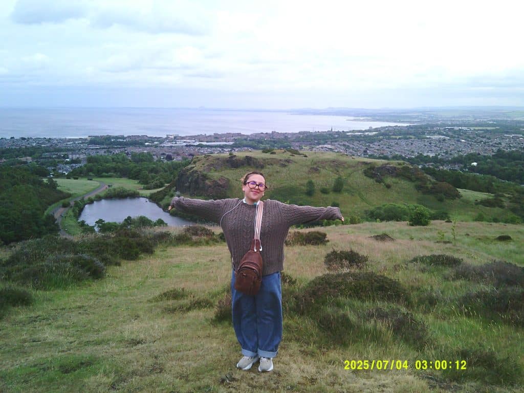 I'm standing on Arthur's Hill in Edinburgh, Scotland, with my arms extended.