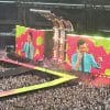 A big screen with a pink and green background with harry styles smiling in front of the colours