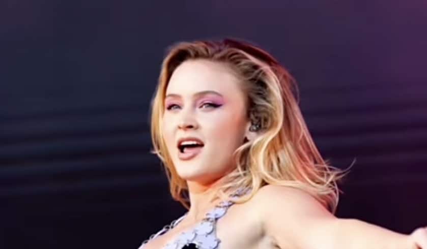 Zara Larsson performs on stage wearing pink eyeshadow, hoop earrings, and a sparkly outfit.