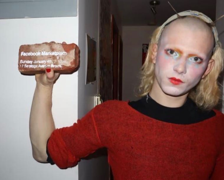 Artist, Solon Perry proudly displays a brick that they have screenprinted. It shows the Facebook Marketplace address in bright white paint.