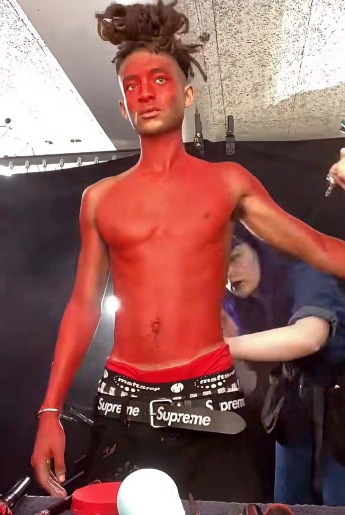 Jaden Smith stands in a makeup room where two assistants are painting his face and body with red paint.