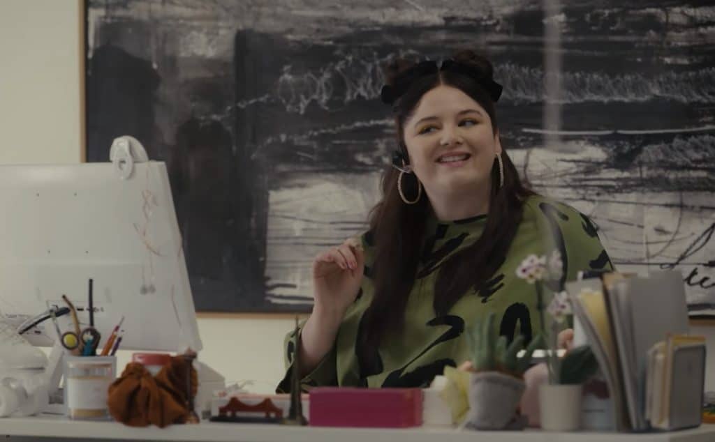 Stalter as Kayla sitting at a desk in a scene from the show Hacks.