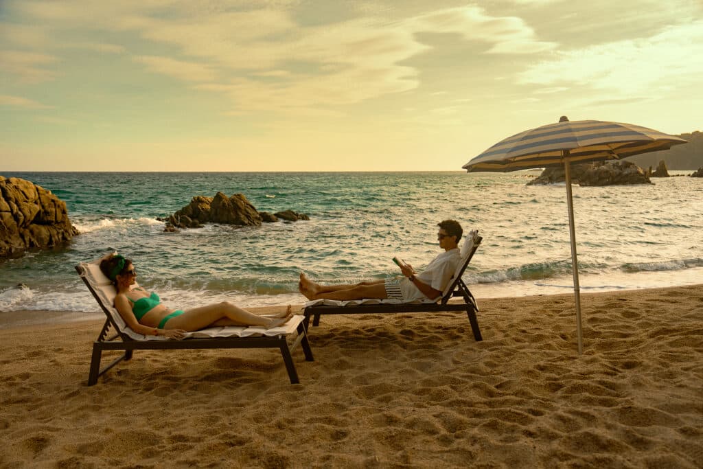 Emily Bader and Tom Blyth sitting and facing each other on a beach for "People We Meet on Vacation."