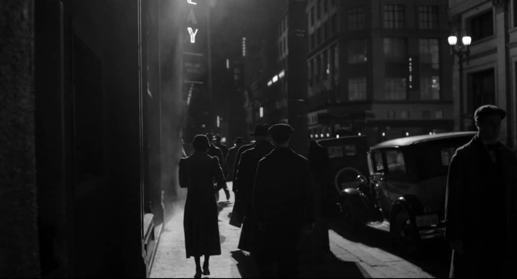 The city of New York at night in black and white, with people walking.