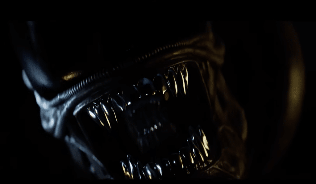 The Xenomorph lunges at the camera. It can be seen to have two sets of sharp teeth.