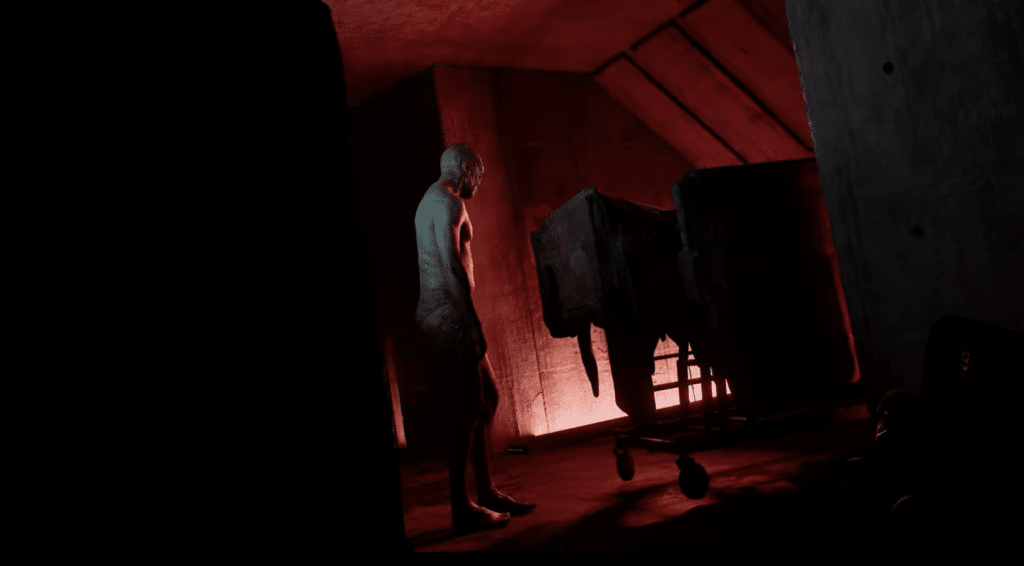 Backlit by eerie red lighting, a zombie stares at the wall while the camera angle indicates the player is crouched, hiding from view.