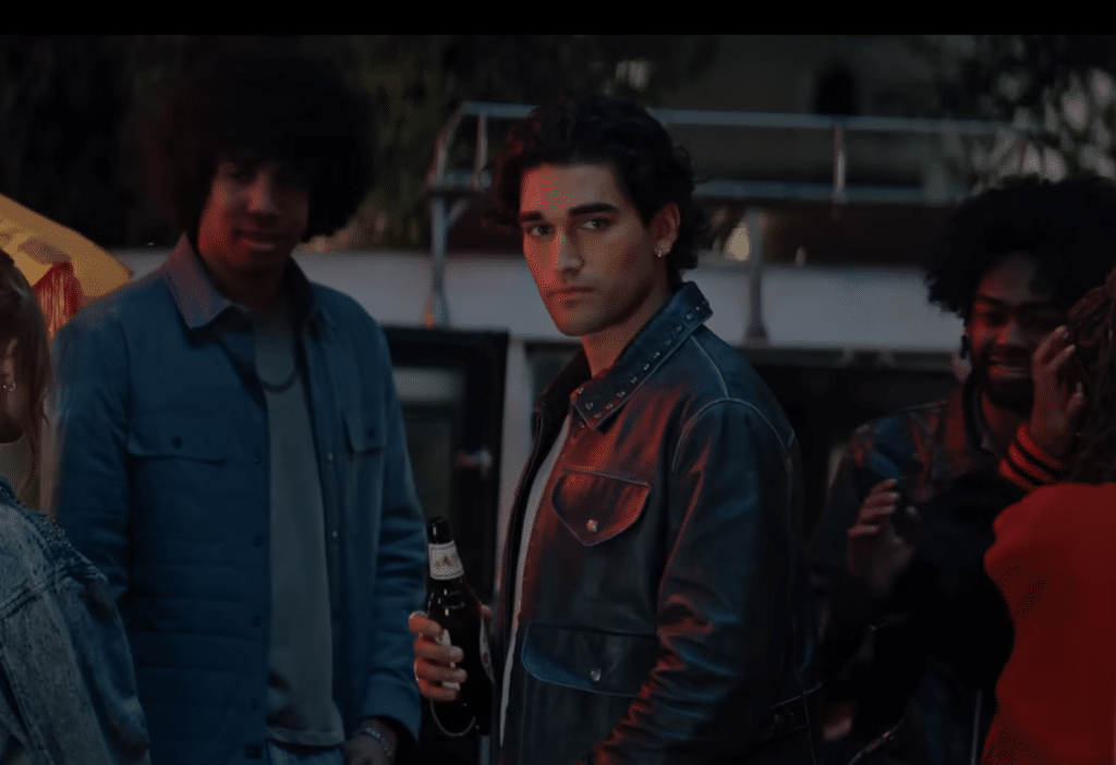 A man in a leather jacket holding a beer staring forwards