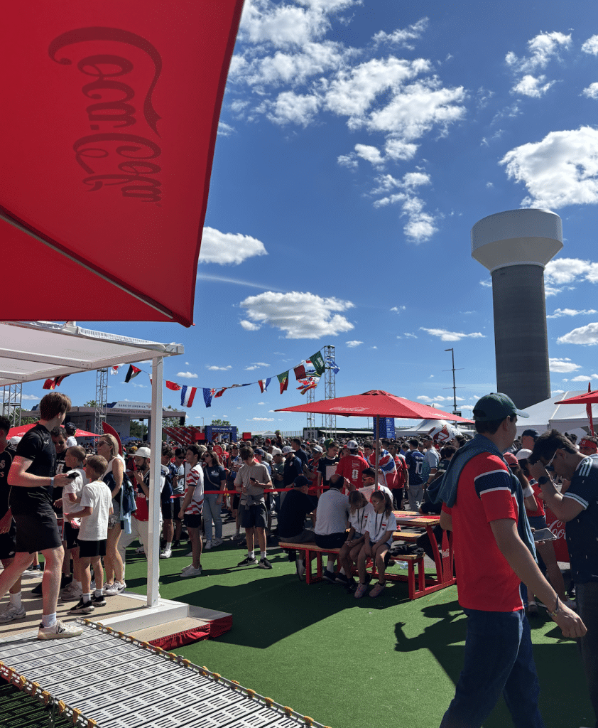 Hundreds of fans sit on picnic tables and huddle under umbrellas as they wait for the match to begin.