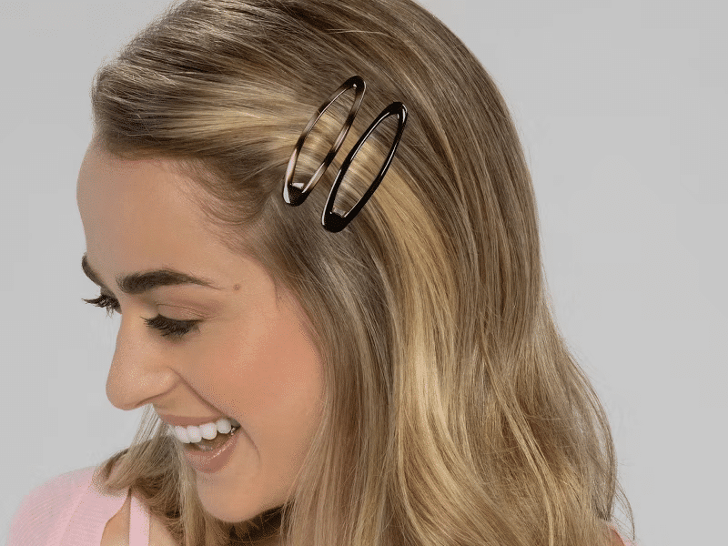 A model is looking to the left, and the camera sees half her head (both face and hair). Her hair is styled with one of each color of the clips to show the colors and what the colors and clips could look like on someone.