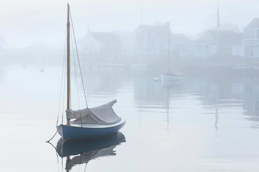 A small blue sailboat in a foggy harbor