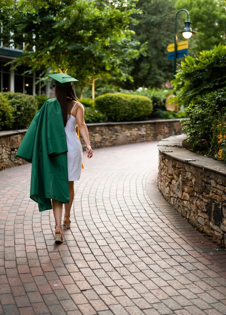 A graduate walks away wearing a cap and gown after commencement.