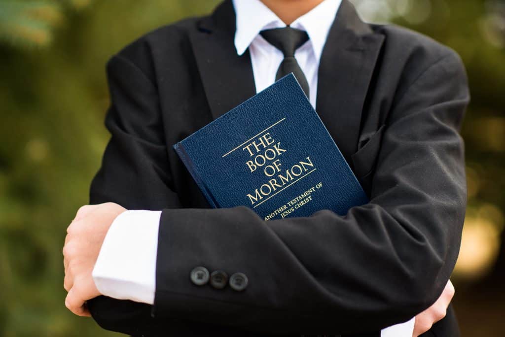 Young man in a suit carrying the Book of Mormon