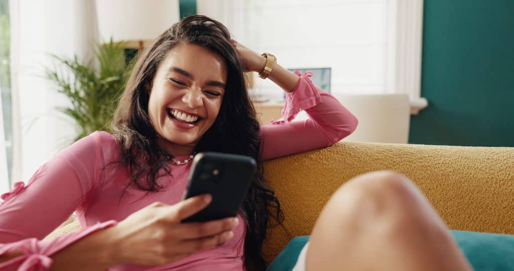 Woman laughing on a couch with a phone in her hand.