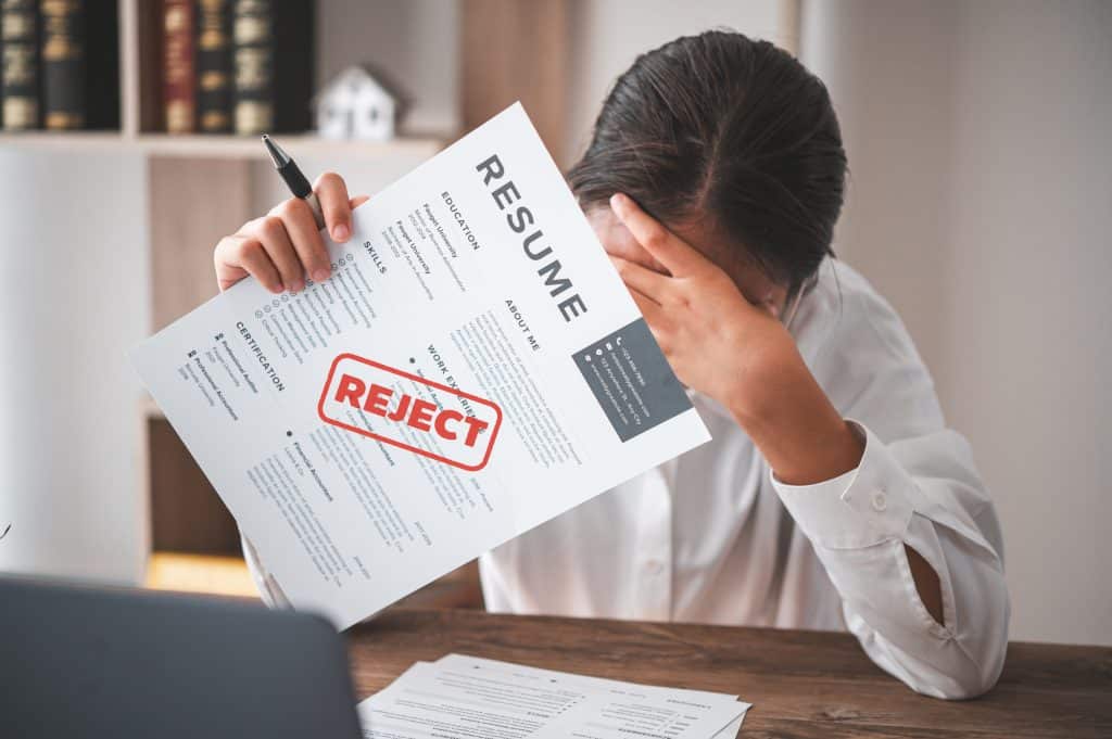 A person holds a résumé marked with a red "Rejected" stamp.