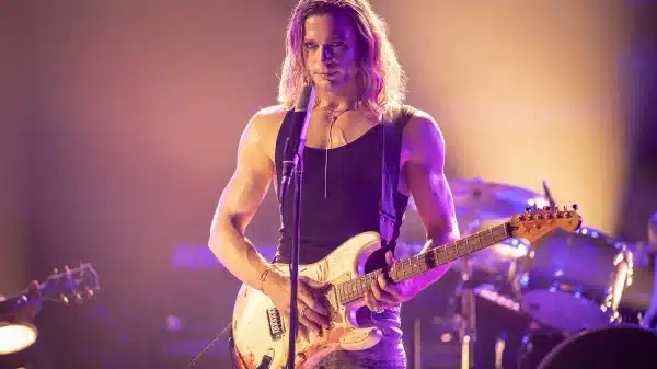 The Vampire Lestat poised in concert, staring down an audience while gripping his guitar.