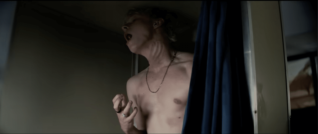 Ryan is cornered in a photobooth struggling, seen with bruises and the imprint of a hand around his throat choking him.