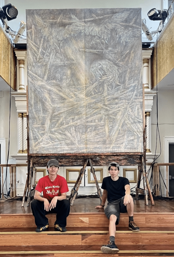 Maverick Mura and Seung-Jun Lee sit in front of Lee's massive painting which towers above them.