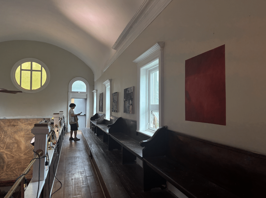 In the rafters of the gallery, a guest looks at a set of paintings.