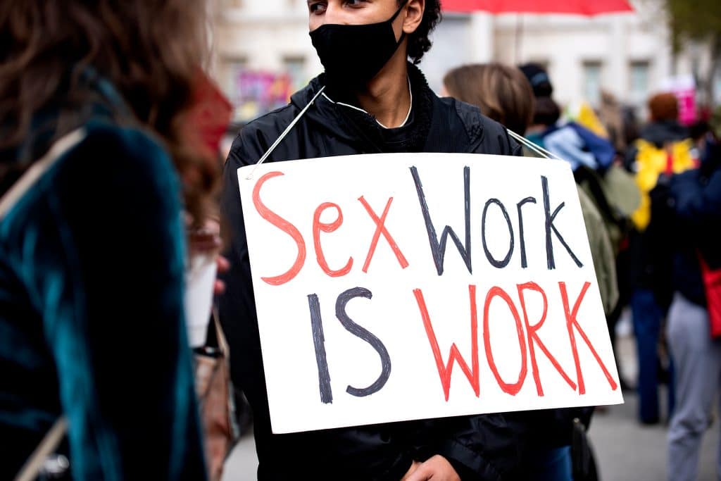 A person stands in a crowd of people holding a sign that says 'sex work is work'
