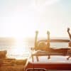 Two women in a convertible car at a beach on the coast of the ocean watching the sunset.