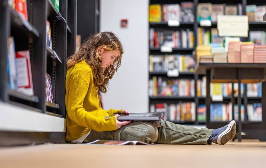 Girl with curly hair and a yellow jumper sat on the floor of a book shop