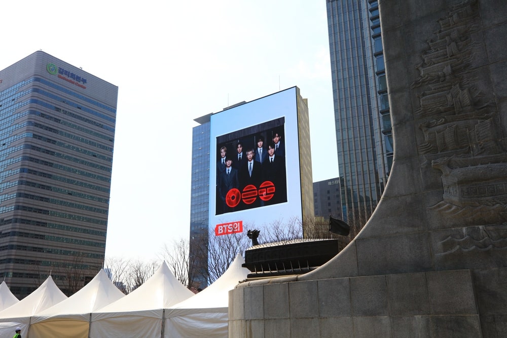 Photo of a billboard promoting a BTS concert amongst other buildings.